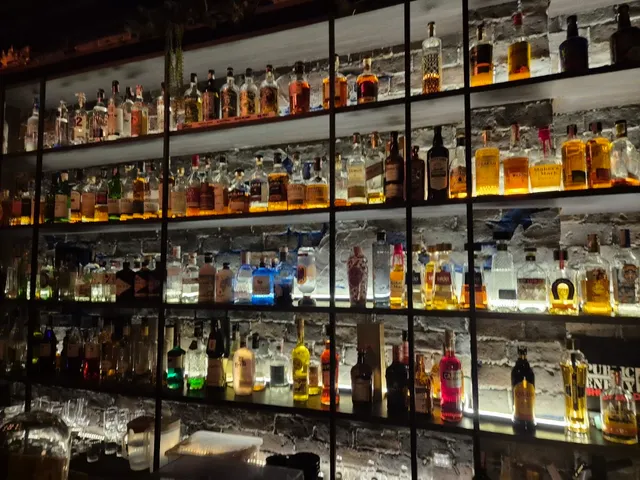 A white brick wall with lit glass shelves packed with liquor bottles