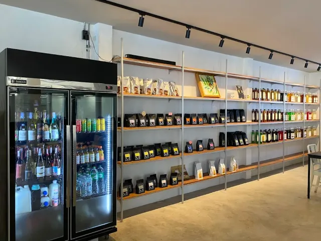 Wooden shelves loaded with coffee bags and bottles, beside a lit drinks fridge