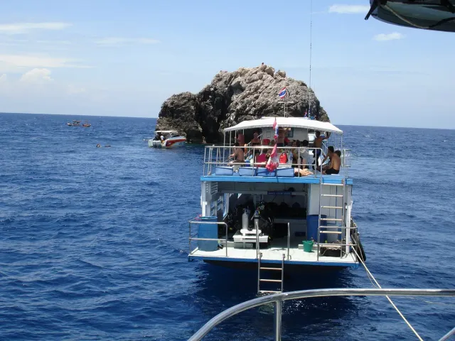 A lone rock rising from deep blue sea with a dive boat moored beside it
