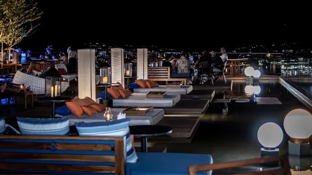 Lounge beds with orange cushions around shallow water on a roof at night