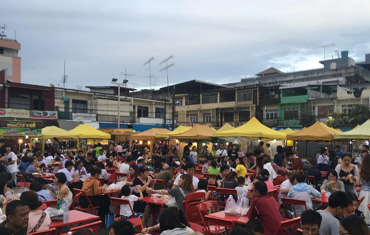 A packed food market with yellow canopies and red tables full of diners at dusk