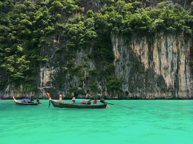 A long tail boat on clear green water between steep limestone walls