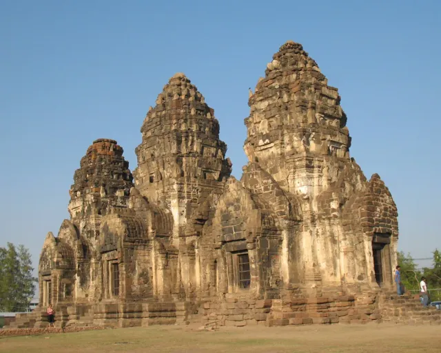 Three linked laterite stone towers on a single base under a blue sky
