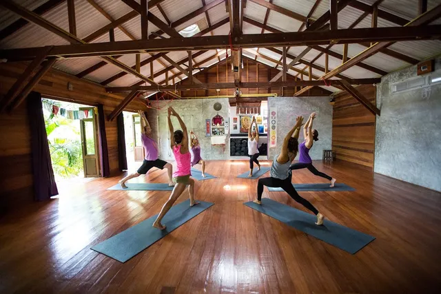 Practitioners in warrior pose on mats in a wooden hall with exposed roof beams
