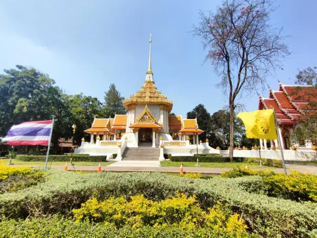 A white and gold pavilion with a pointed spire surrounded by tended gardens and flags