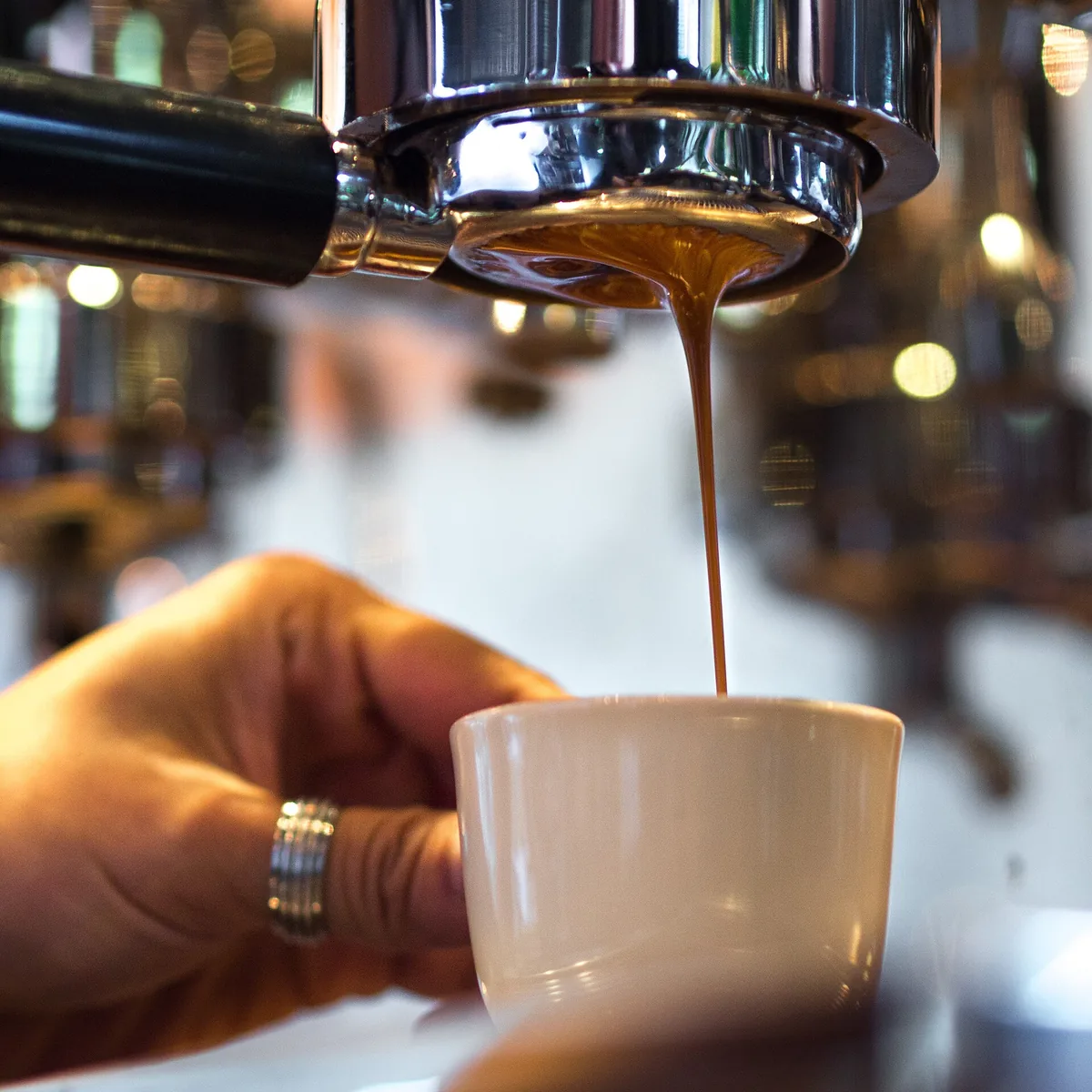 Espresso pulling from a naked portafilter into a white cup, against a blurred cafe background
