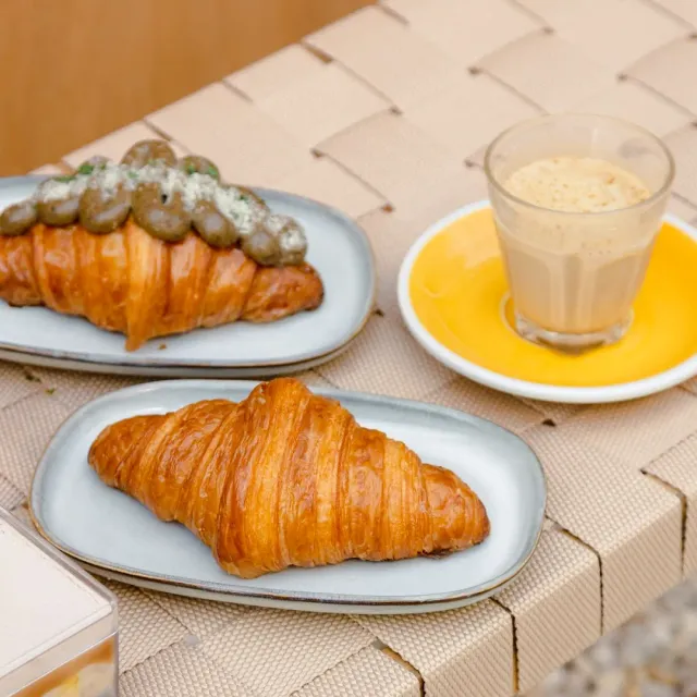 Two croissants on plates, one with a savory filling, and a glass of iced coffee beside them