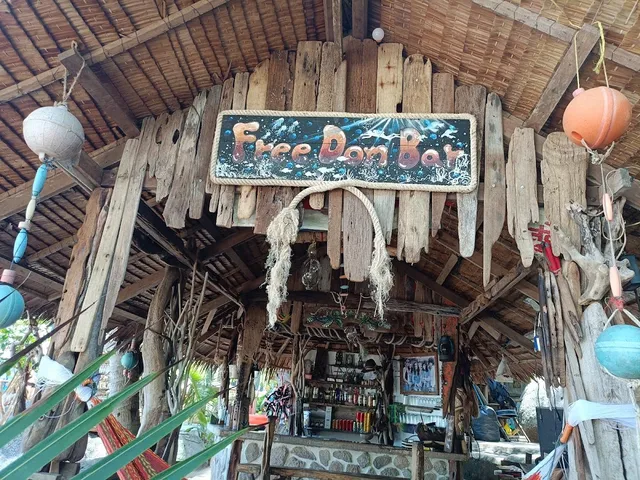 A driftwood bar with a thatched roof, a painted sign and hanging floats