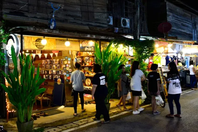 A lit souvenir shop in an old wooden house, passersby walking along the sidewalk in the evening