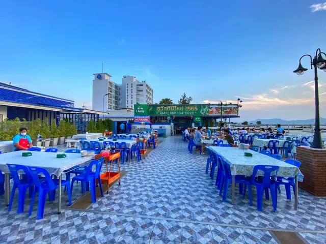 An open terrace with square tables and blue plastic chairs facing the waterline