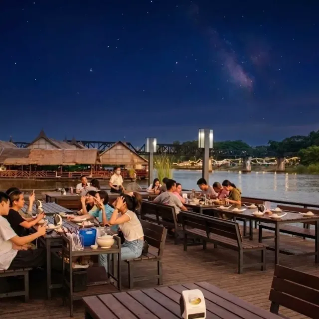 A wooden terrace above the water at night with many diners and a starry sky above