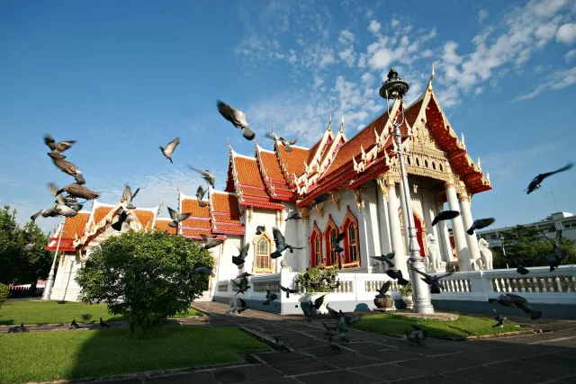 A white marble temple with orange tile roofs and a flock of pigeons flying above it