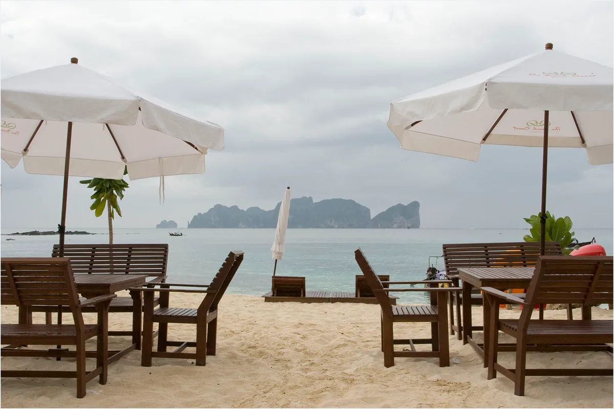 Wooden tables and white parasols on the sand facing the sea with an island cliff on the horizon