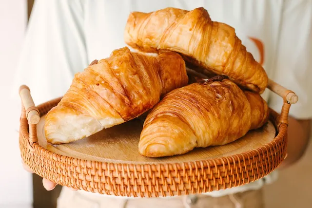 Three golden croissants on a round wicker tray with handles