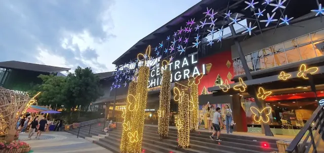 A mall facade at dusk, light columns and illuminated butterflies above the stairs