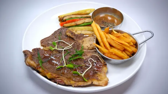 A white plate with steak cuts, sauteed vegetables, fries and sauce in a small metal cup