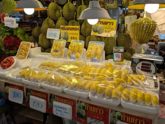 A fruit stall piled with whole durians and packed durian trays with price signs