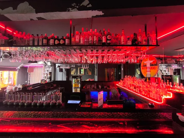 A red-lit bar counter with hanging glasses and bottle shelves above it