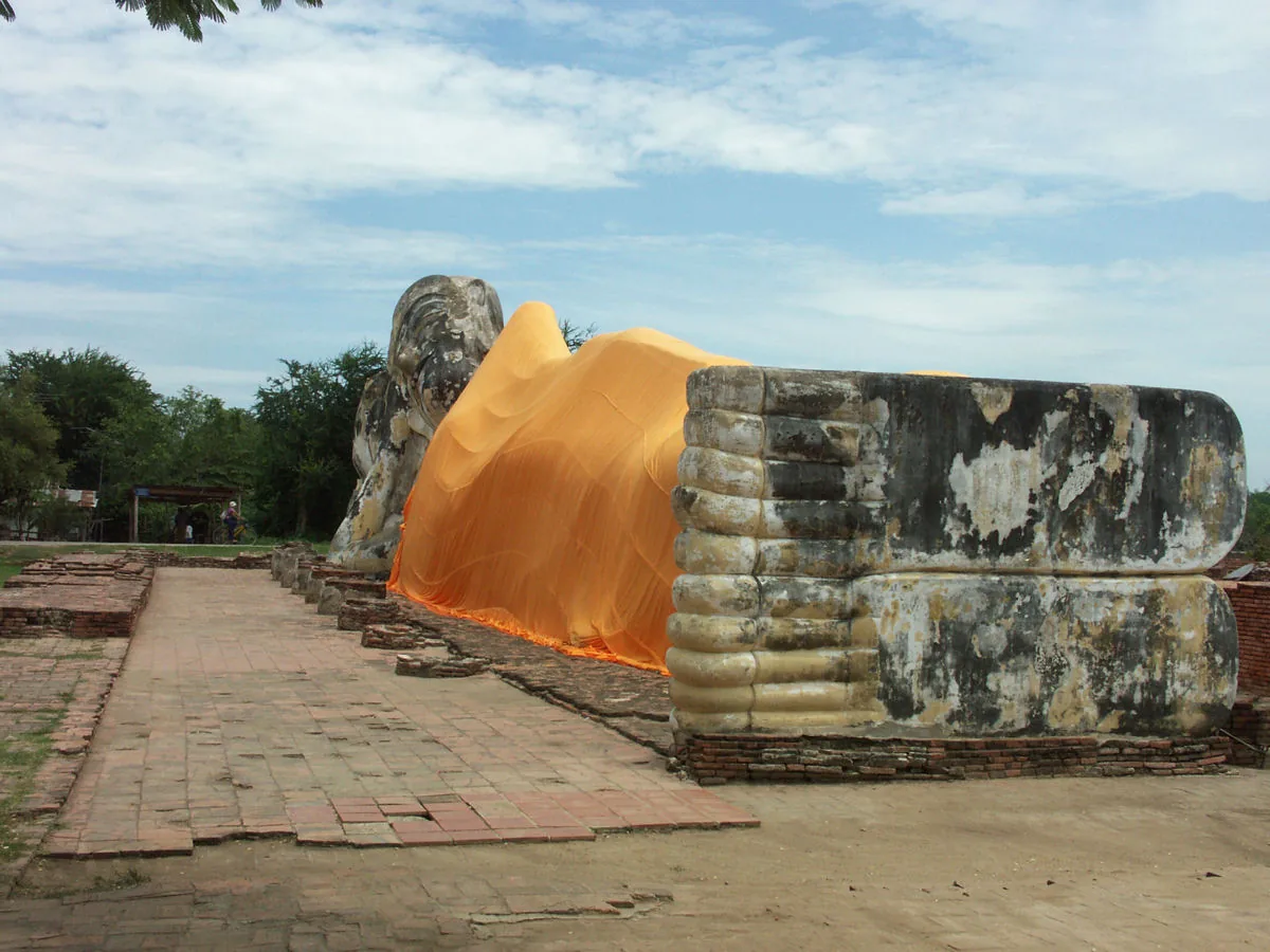 A giant reclining Buddha wrapped in an orange robe, on an open brick terrace