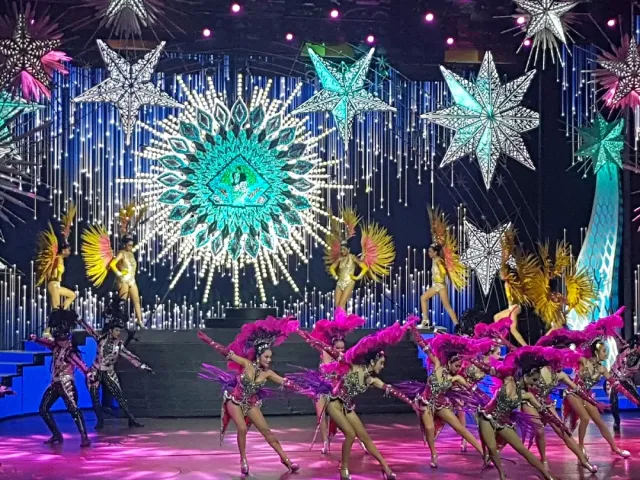 Dancers in pink and gold feathers on stage against glittering star lights