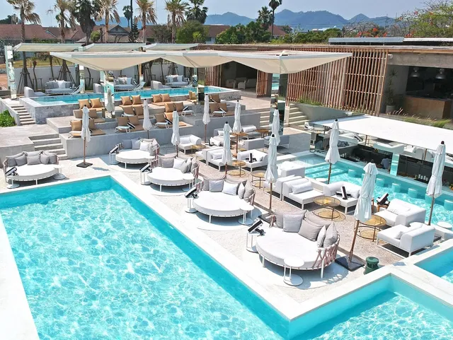 A white pool complex with round sunbeds and parasols, with mountains in the background