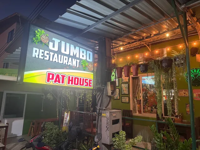 A lit sign above a restaurant front with hanging plants and a string of lights