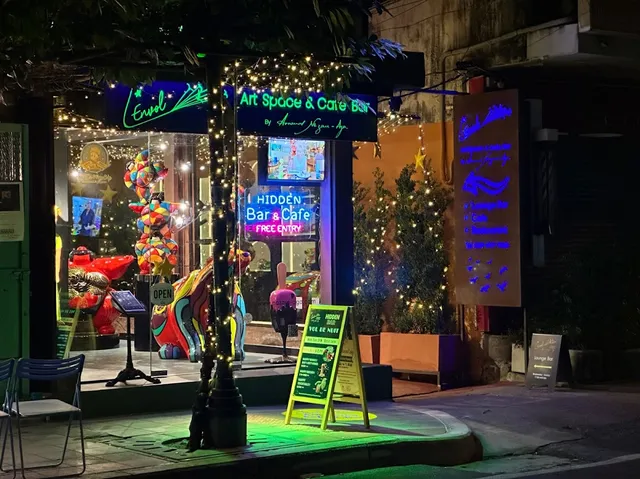A frontage lit with string lights and neon at night, with colorful sculptures in the window and a sidewalk sign