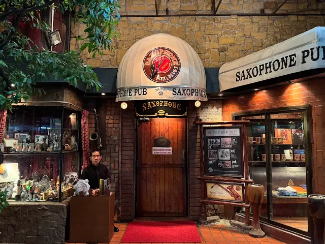 An entrance with white awnings, a brick wall, a red carpet and a man standing at the door