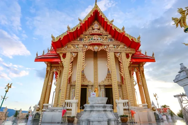 A gilded prayer hall with a tiered red roof and a marble staircase at the front