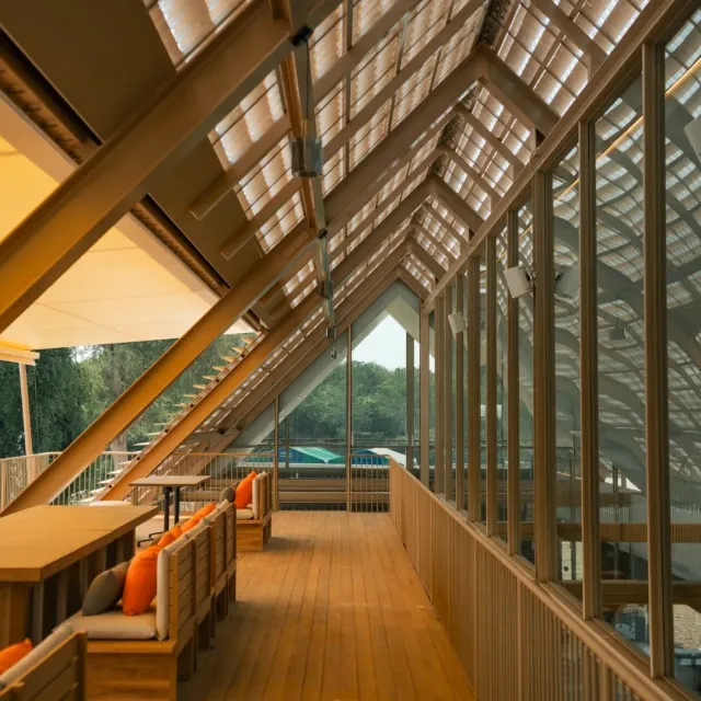 A long terrace under a sloped roof with a glass wall, benches and orange cushions