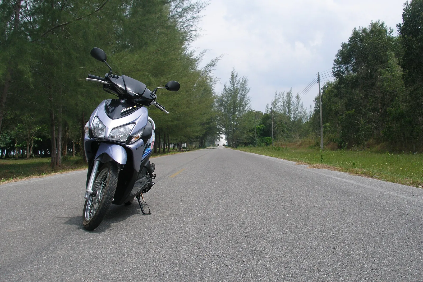 A scooter parked beside an open road in Thailand