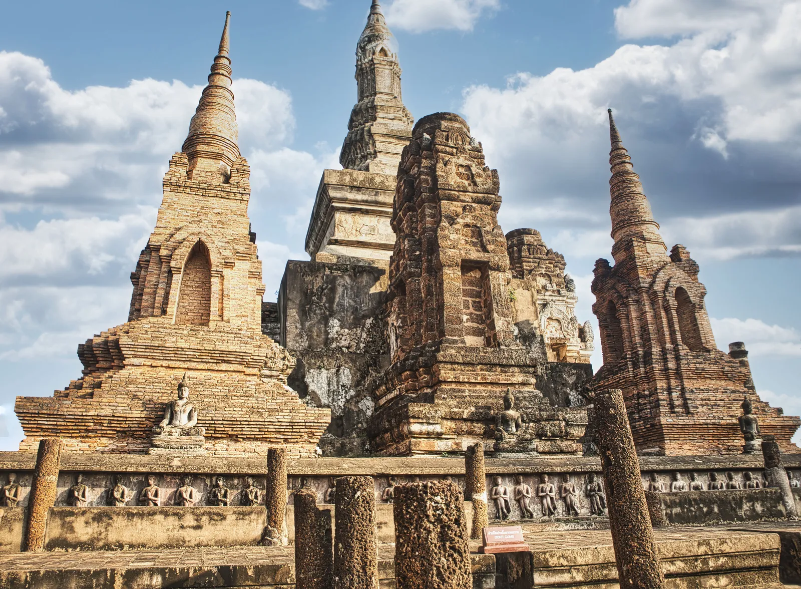 A row of standing Buddha statues on a raised brick platform at Wat Mahathat, Sukhothai, Thailand