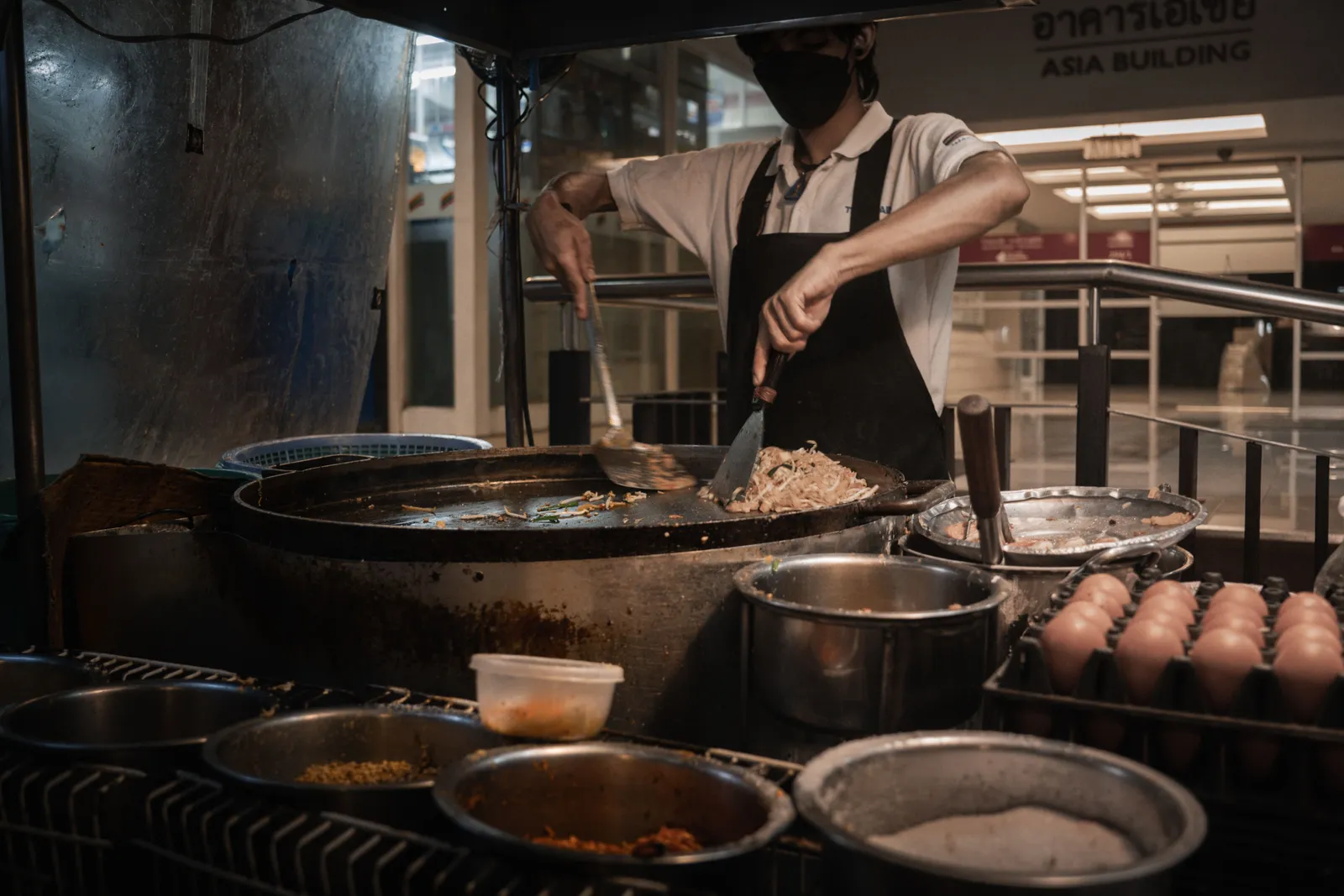 A cook stir frying in a large wok at a Thai food stall