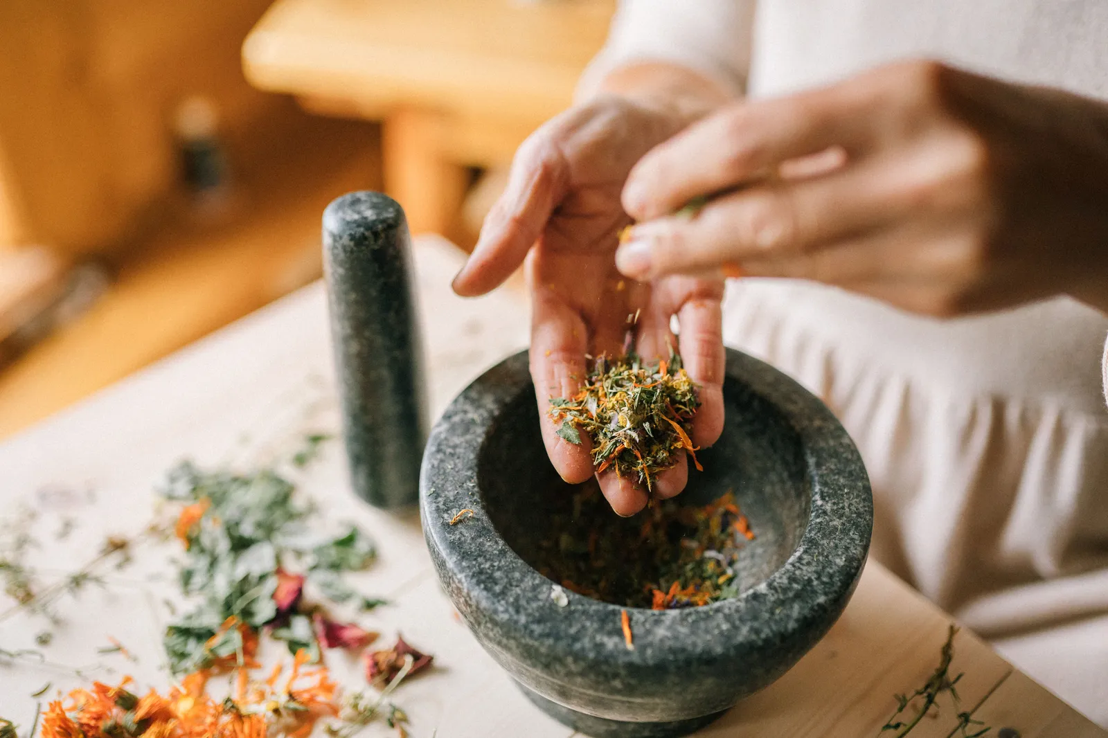 A granite mortar and pestle with fresh herbs and chillies being pounded into Thai curry paste