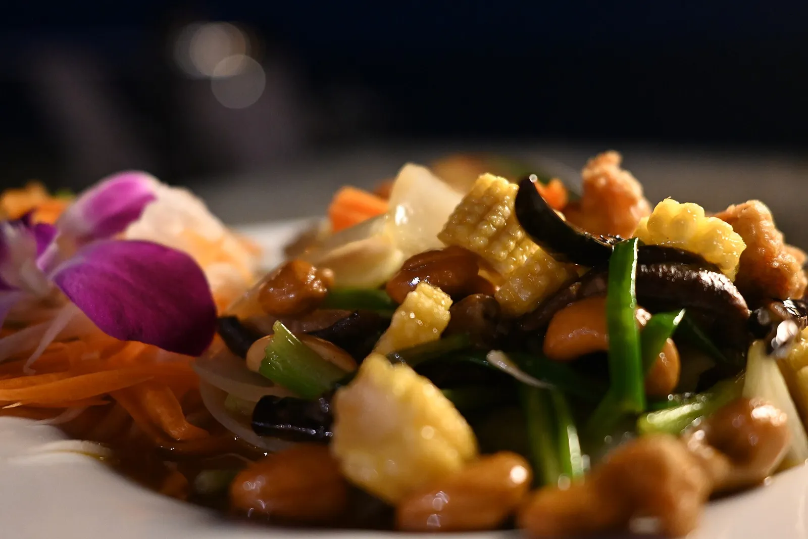 A colourful Thai-style vegetable stir-fry with baby corn, cashews and peanuts, garnished with an edible orchid, a vegetarian dish with no meat or fish