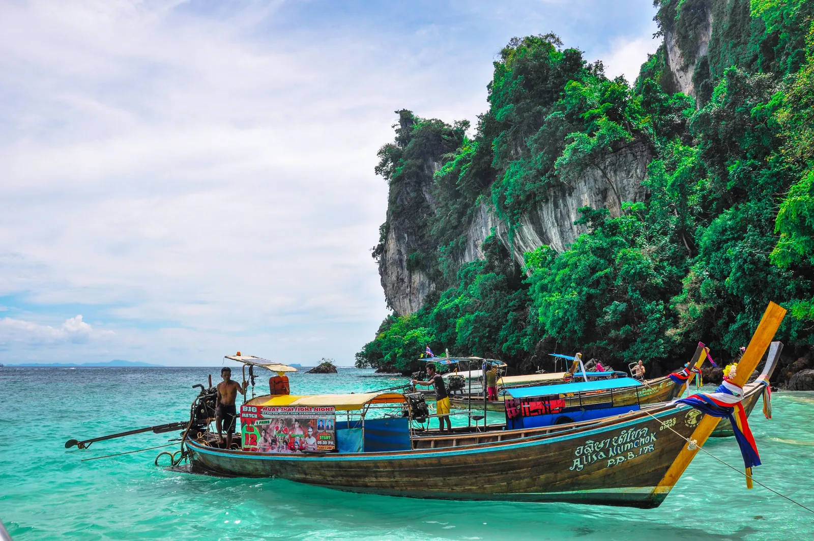 A longtail boat on turquoise water beside limestone cliffs on the Andaman coast of Thailand