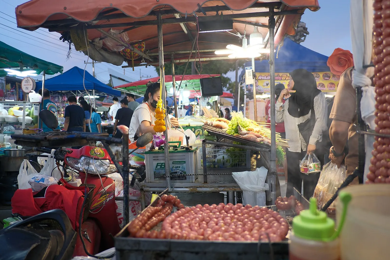 A busy evening market food stall with fresh produce and cooked snacks in Thailand