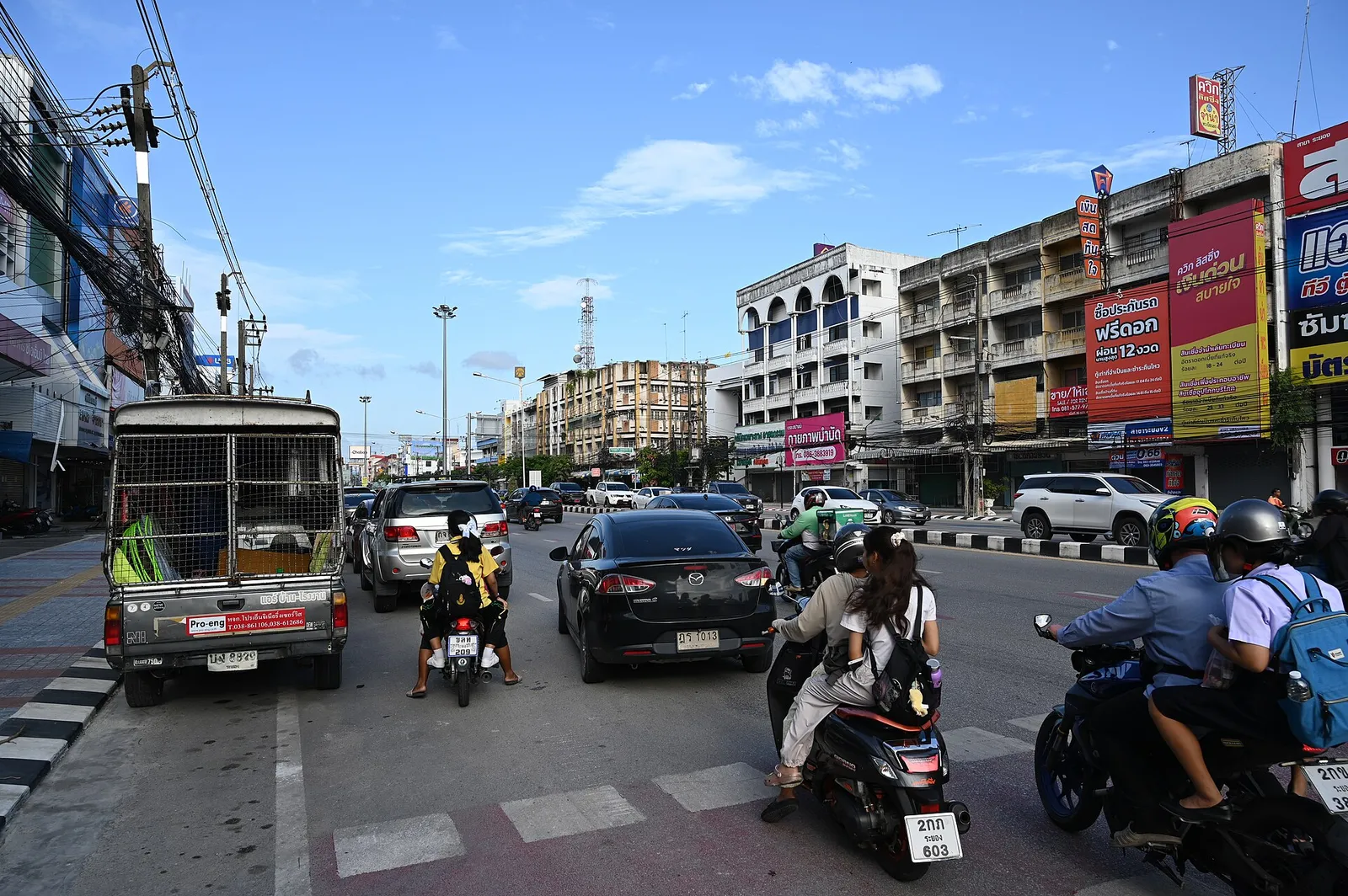A busy Thai street with motorbikes and local traffic under a bright sky