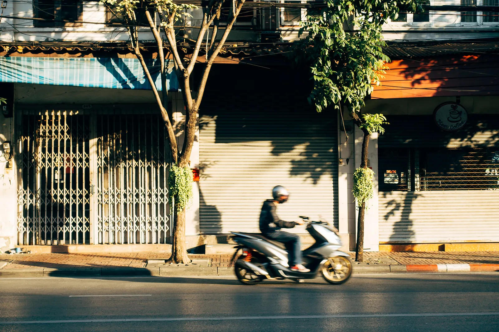 A shuttered shopfront on a Bangkok street in daylight, with pedestrians passing on the pavement