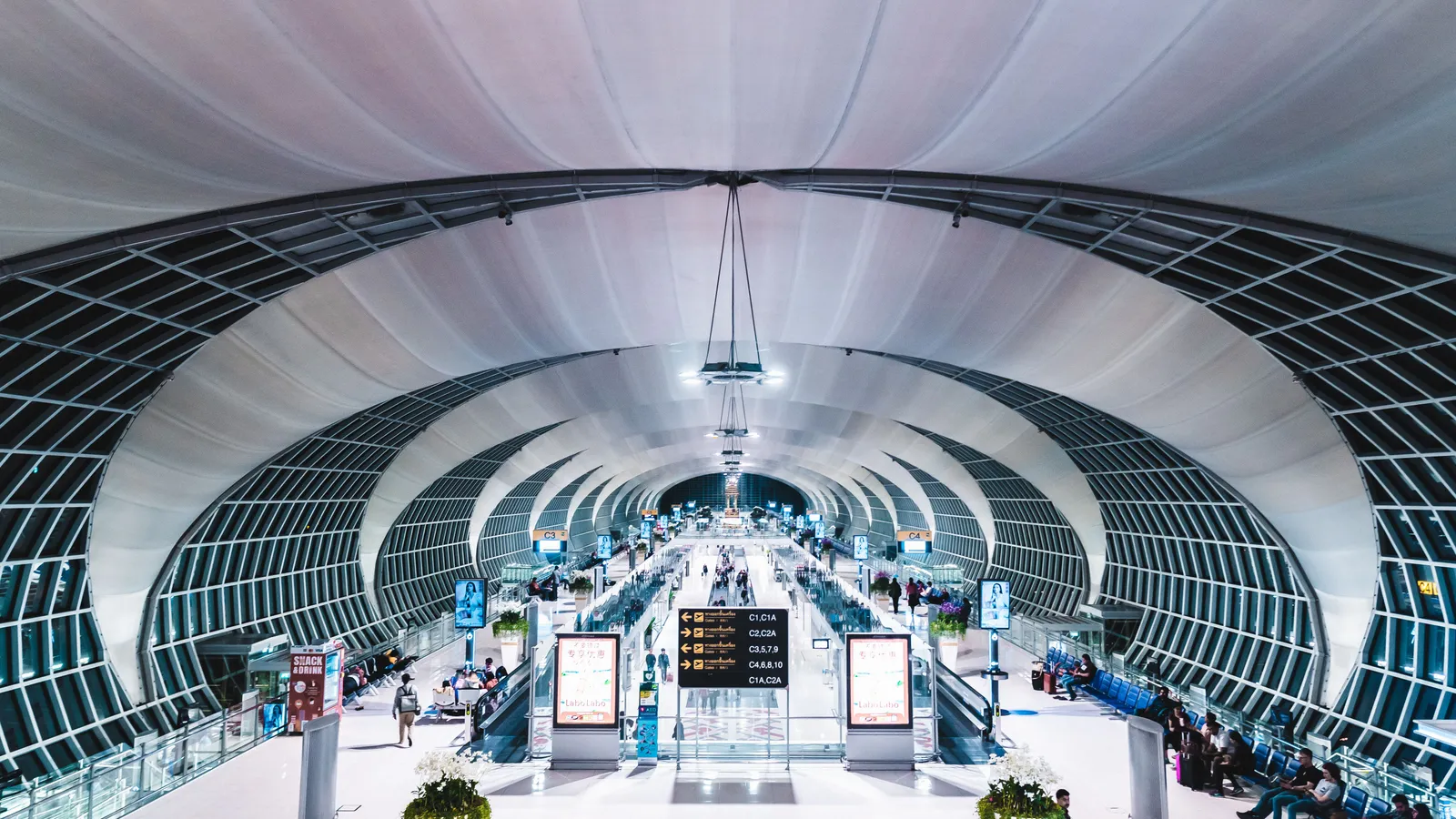 The departure hall of Suvarnabhumi Airport in Bangkok, Thailand, with travellers under the curved roof