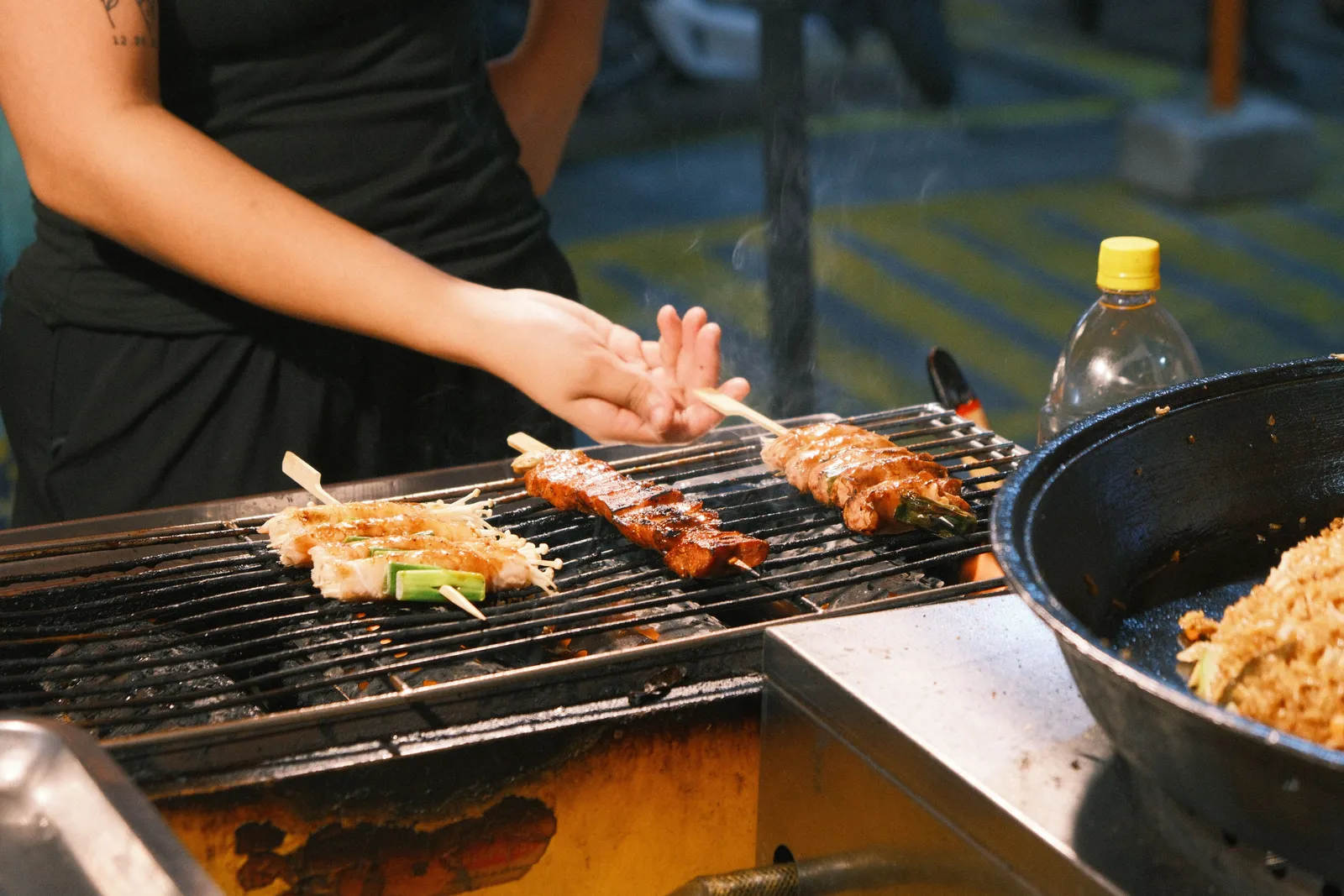 A street food vendor grilling skewers over charcoal on Yaowarat Road at night