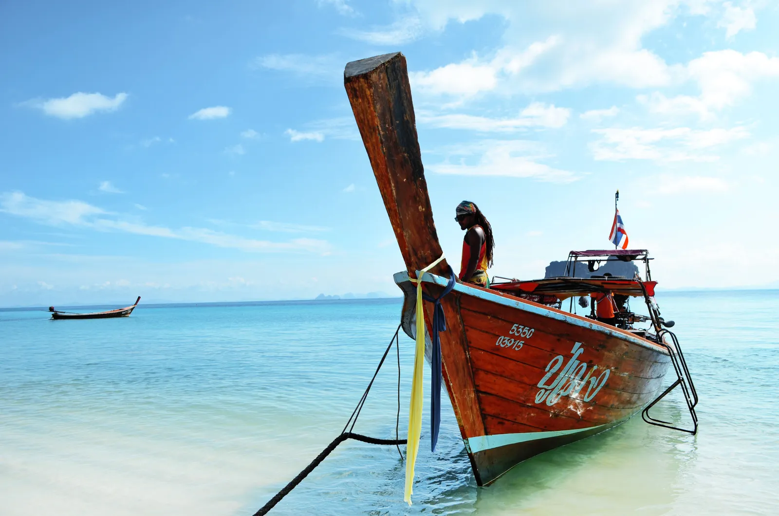 A private longtail boat anchored near an empty white sand beach in southern Thailand