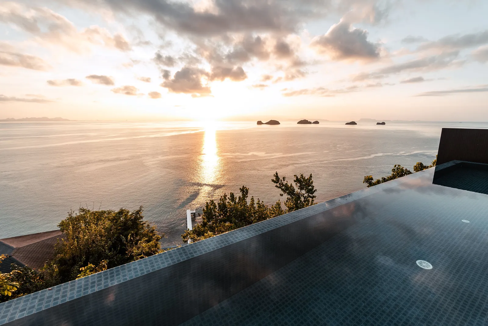 An infinity pool at sunset looking out over the sea towards distant offshore islands