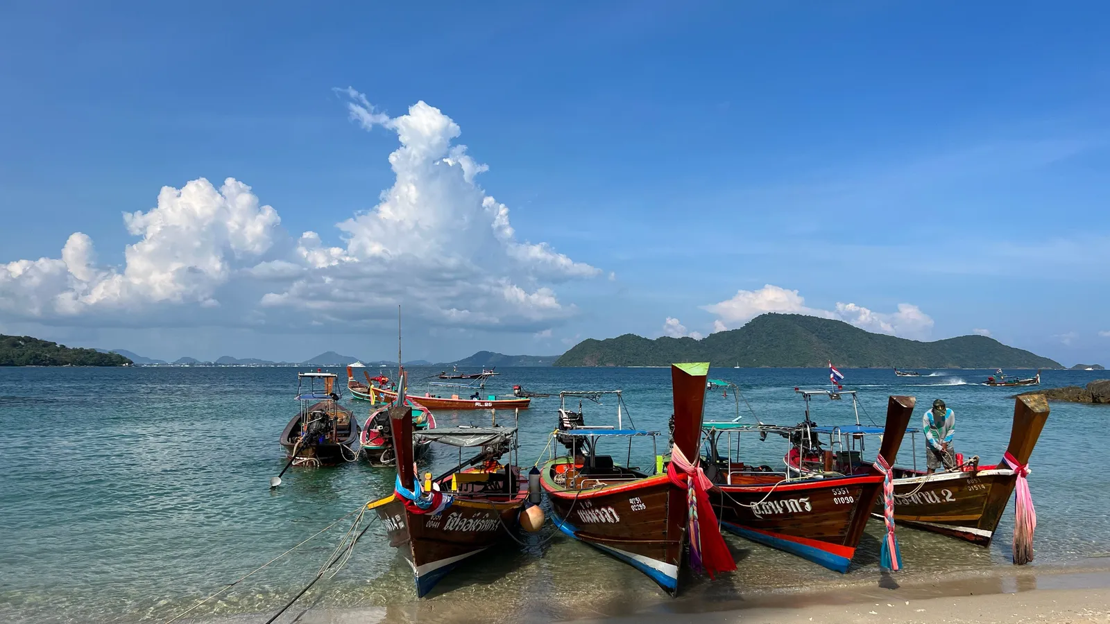 A quiet family beach with longtail boats moored offshore on the Andaman coast of Thailand